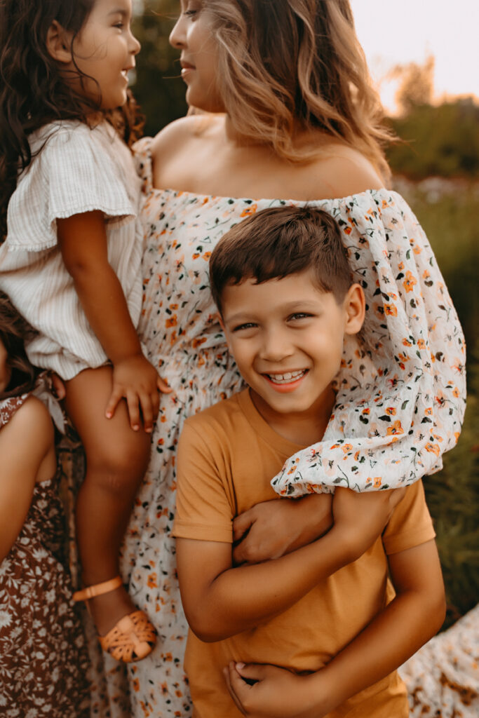 Mother holding her daughter and wrapping her arm around her young son who is grinning.