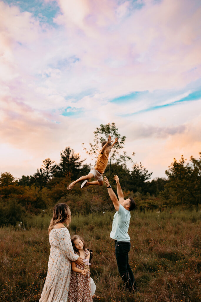 Father throwing his son up in the air while his mother and sister look on. 